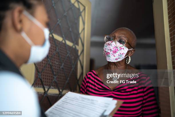 topógrafo hablando con la mujer mayor en la puerta - usando máscara facial - petición fotografías e imágenes de stock