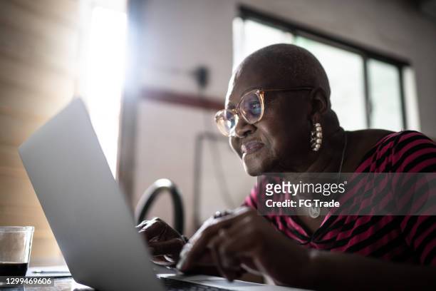 seniorin mit laptop zu hause - learning resources for reading stock-fotos und bilder