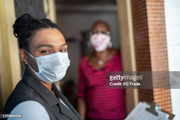 portrait of female surveyor in the doorstep of a senior woman house - wearing face mask - social worker mask stock pictures, royalty-free photos & images