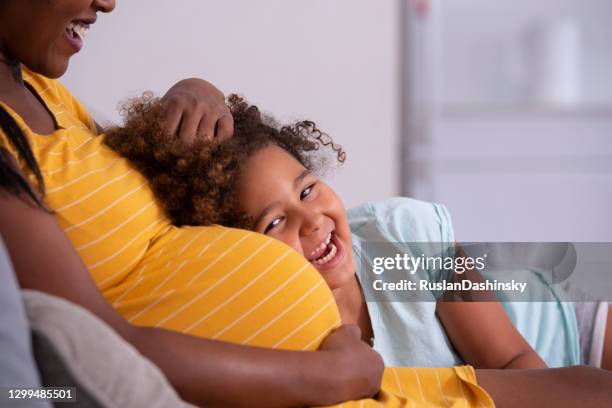 happy little mixed-race girl leaning against pregnant mother's belly. - little kids belly imagens e fotografias de stock