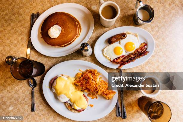 pancakes, fried eggs with bacon and eggs benedict with ham and hash brown served at a traditional american diner, high angle view - hash brown stock pictures, royalty-free photos & images