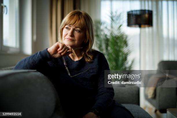 portrait of worried senior woman sitting on sofa at home - guilt stock pictures, royalty-free photos & images