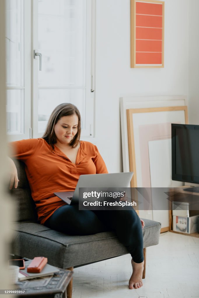 Glimlachende Plus Size Vrouw die comfortabel in een Leunstoel zit en aan laptop werkt