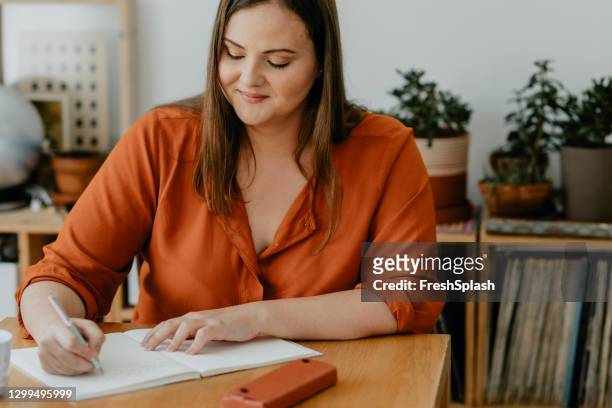 mooie zitting van de te zware vrouw in haar woonkamer en het schrijven van een dagboek - diary stockfoto's en -beelden