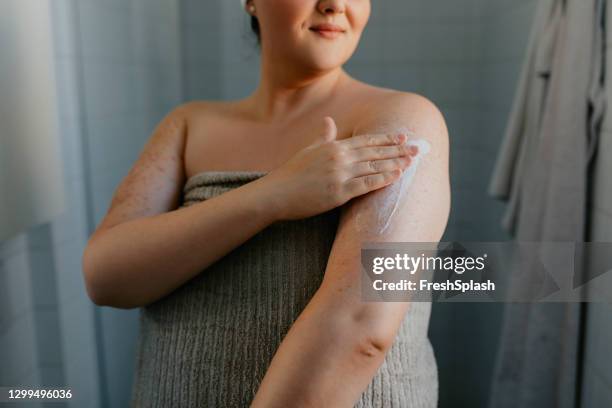 mujer con sobrepeso anónima aplicando loción corporal después de la ducha - crema fotografías e imágenes de stock