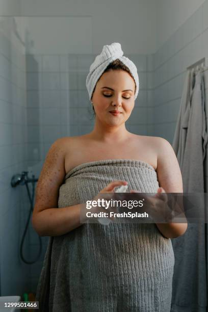 glimlachende plus size vrouw die de lotion van het lichaam na het nemen van een douche toepast - hair conditioner stockfoto's en -beelden