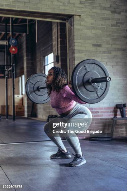 determined young woman lifting barbell at gym - black female bodybuilder stock-fotos und bilder