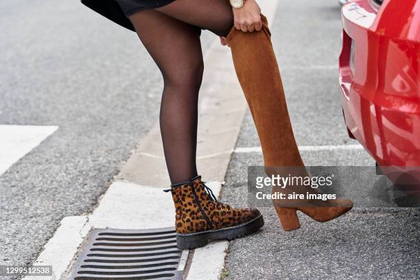 woman changing her footwear while standing next to her car outdoors on the street. - stiefel stock-fotos und bilder
