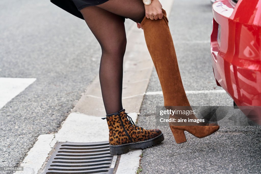 Woman changing her footwear while standing next to her car outdoors on the street.