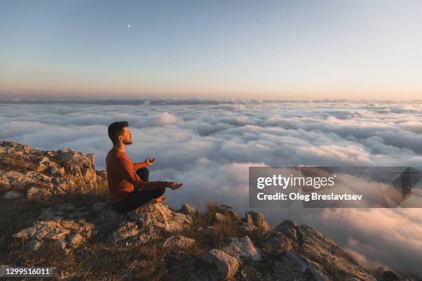 man meditating alone in mountains with amazing sunrise view of low clouds. awakening and harmony with nature. - man doing yoga in the morning stockfoto's en -beelden