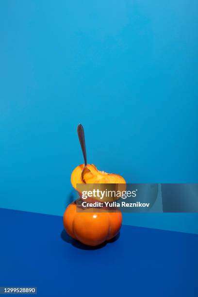 fuyu persimmons (khaki fruits) with spoon on the blue background - kaki stockfoto's en -beelden