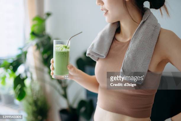 close up of confidence young asian sports woman taking a break, refreshing with healthy green juice after fitness work out / exercising / practicing yoga at home in the fresh bright morning - detox stock pictures, royalty-free photos & images