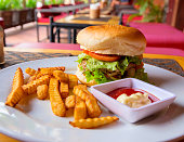 Hamburger, french fries, mayonnaise and ketchup on restaurant background. Yummy fresh burger and french fries on white plate served for lunch. Rich kids food menu closeup photo. Nutritive breakfast.