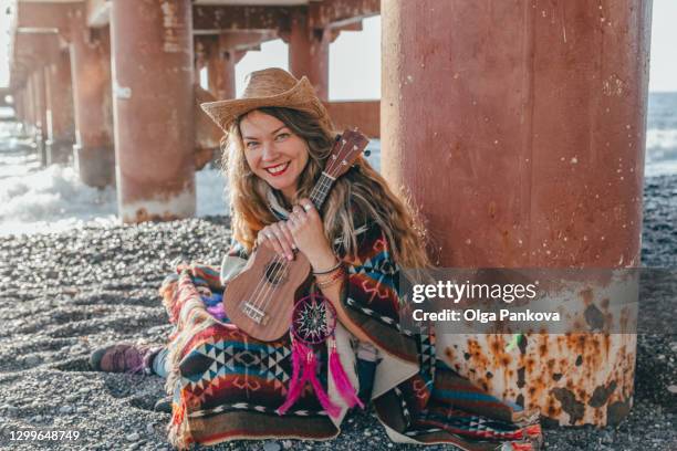 a hippie young woman sits on the beach near the pier and plays the ukulele. - hippie bildbanksfoton och bilder