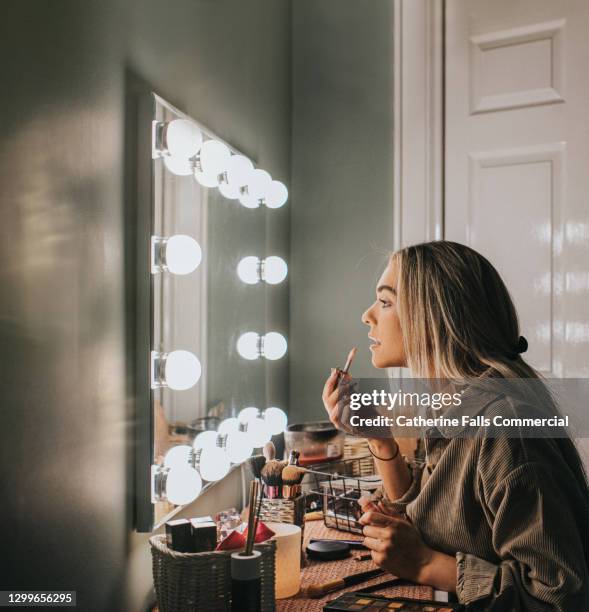 a woman stares into an illuminated mirror as she concentrates while applying lipgloss - kaptafel stockfoto's en -beelden