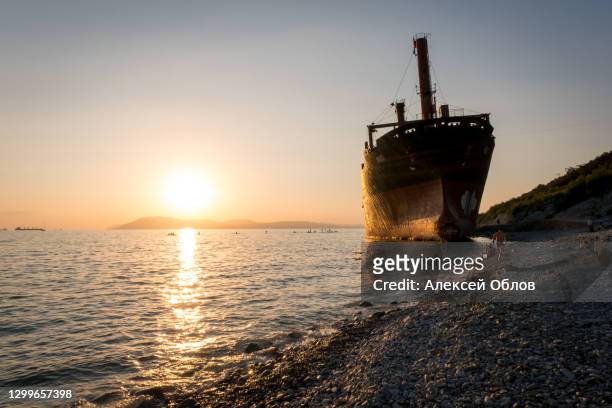 cargo ship running aground. sunset on the pebbly seashore - schlepper stock-fotos und bilder