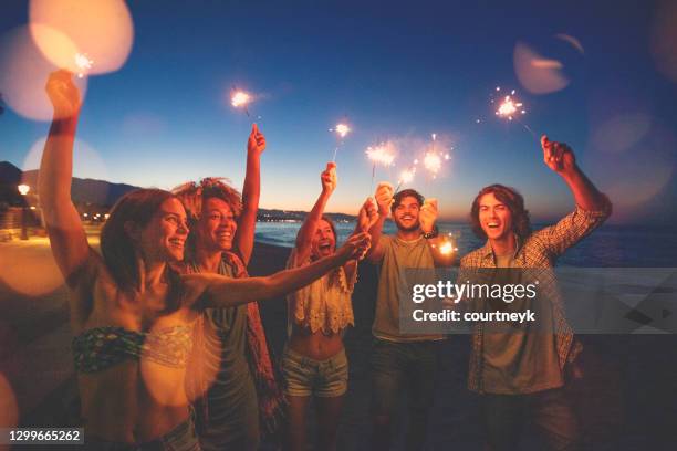 groep vrienden die met sterretjes en vuurwerk op het strand bij zonsondergang spelen. - provincie málaga stockfoto's en -beelden