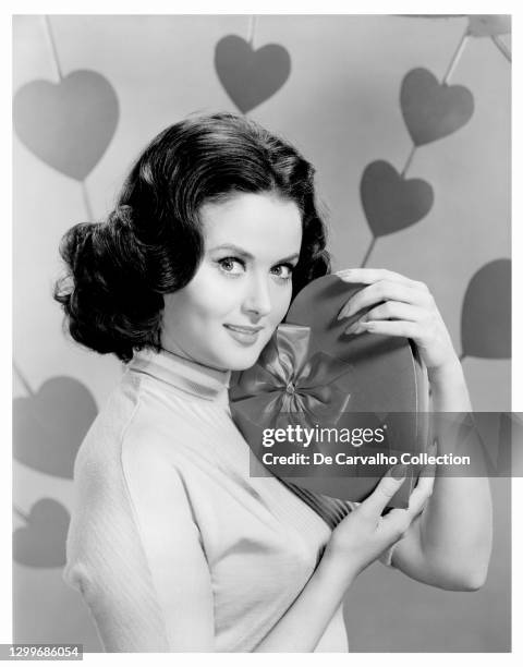 Actress and Model Nancy Walters holds a heart-shaped box of chocolate on Valentine’s Day in a publicity shot from the the early 1960's, United States.