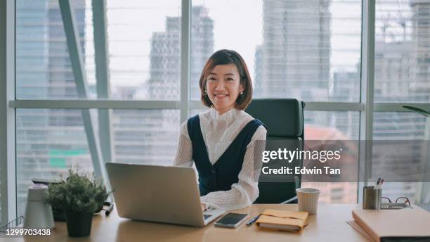 asiatiska kinesiska vackra kvinna vd högsta ledningen tittar på kameran leende på hennes skrivbord i office - generalsekreterare företagsledning bildbanksfoton och bilder