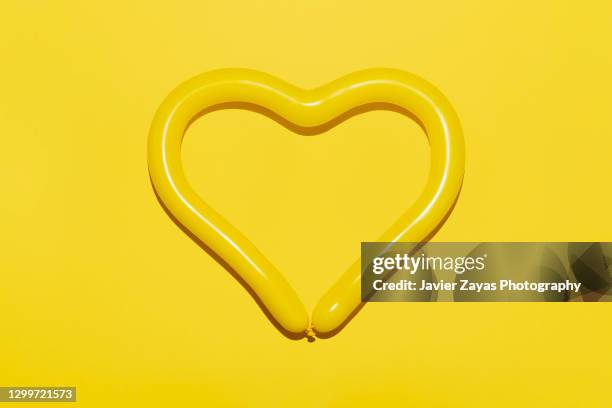 heart shaped yellow balloon against yellow background - balloon knot stock pictures, royalty-free photos & images