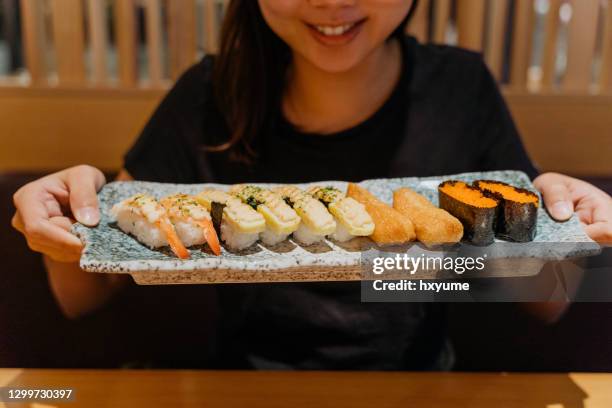 smiling young asian woman holding a plate of sushi set - sushi restaurant stock pictures, royalty-free photos & images