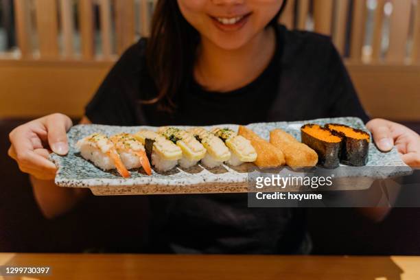 面帶微笑的年輕亞洲女人拿著一�盤壽司 - sushi restaurant 個照片及圖片檔