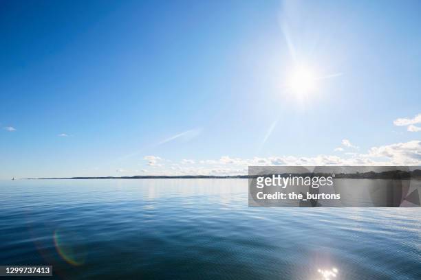 full frame shot of smooth sea and blue sky against sunlight - back lit clouds stock pictures, royalty-free photos & images
