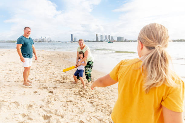 family spends time at the beach playing together on the sand - beach cricket australia stock pictures, royalty-free photos & images