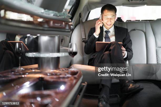 asian businessman using tablet in luxury car and making a call - asian man car stock pictures, royalty-free photos & images