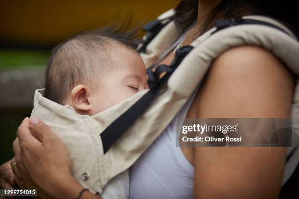 close-up of mother carrying sleeping baby in baby carrier - babytrage stock-fotos und bilder