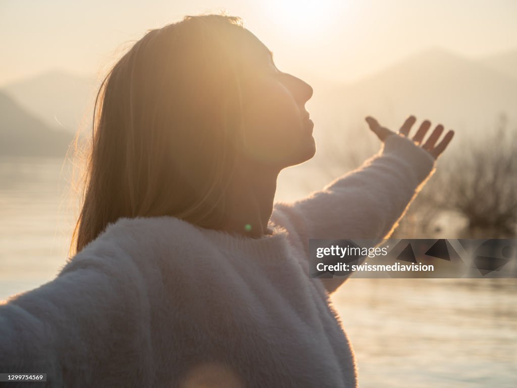 Frau umarmt die Natur, sie steht arme am See bei Sonnenuntergang
