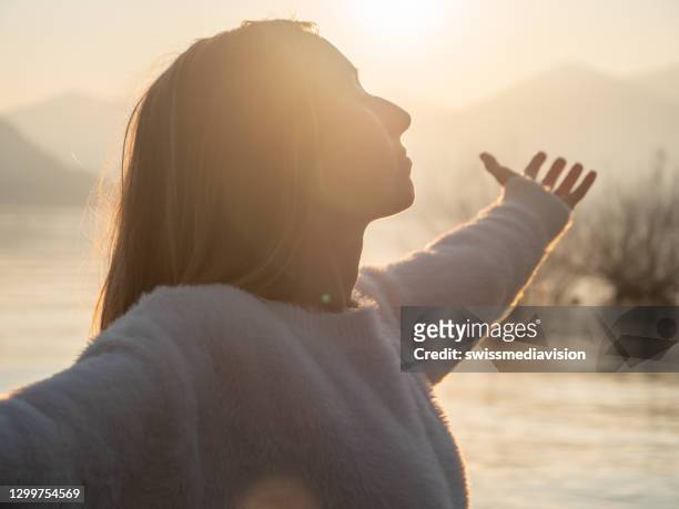 woman embraces nature, she stands arms out by the lake at sunset - holistic medicine stock pictures, royalty-free photos & images