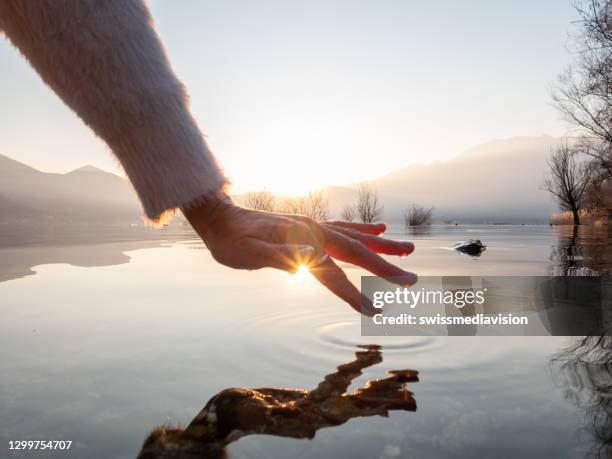 detail van hand die wateroppervlakte van meer bij zonsondergang raakt - new life stockfoto's en -beelden