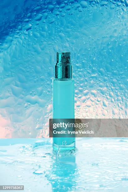 beauty product with transparent liquid as a skin moisturizer on a blue background with splashes and water drops. - bottle condensation stock pictures, royalty-free photos & images