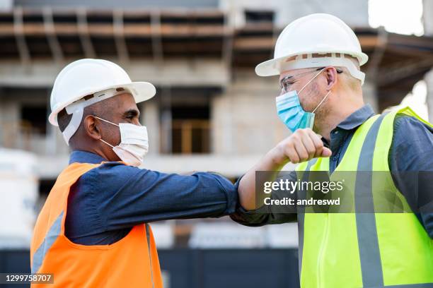 men working on construction, new greeting using coronavirus face protection mask - touching elbows stock pictures, royalty-free photos & images