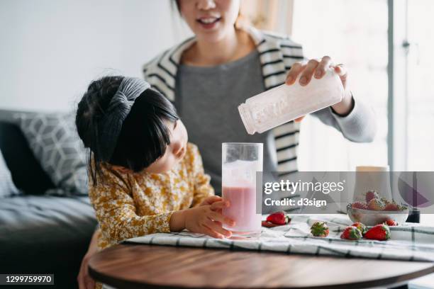 young asian mother making healthy strawberry smoothie with fresh fruit with lovely little daughter at home. little daughter is excited about the drink while mother is pouring to glass. healthy eating and healthy lifestyle - stoffwechsel entgiftung stock-fotos und bilder