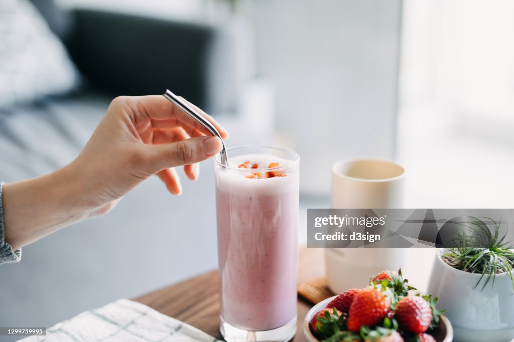 Close up of young woman drinking a glass of fresh and healthy strawberry smoothie with reusable metal straw. Healthy eating and healthy lifestyle