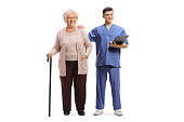 Full length portrait of a male nurse with a clipboard and an elderly female patient with a walking cane