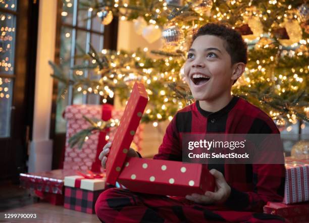 chico adolescente de carrera mixta que abre regalos de navidad - christmas gift fotografías e imágenes de stock