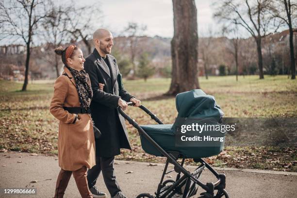 young parents walking with baby carriage in park - baby pram in the park stock pictures, royalty-free photos & images