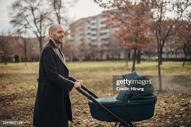 young father taking a walk with baby carriage in park - stroller stock pictures, royalty-free photos & images