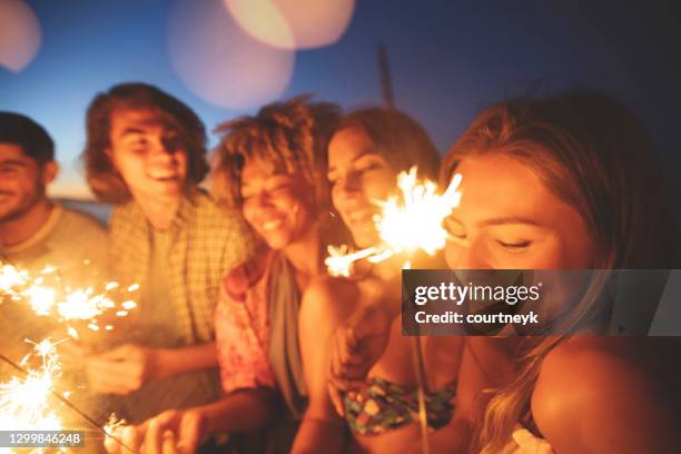 groep vrienden die met sterretjes en vuurwerk op het strand bij zonsondergang spelen. - beach night stockfoto's en -beelden