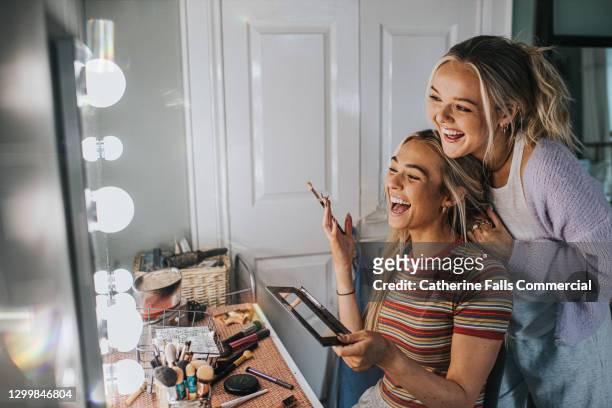 two young woman front of an illuminated mirror and apply make-up - friends women makeup stockfoto's en -beelden