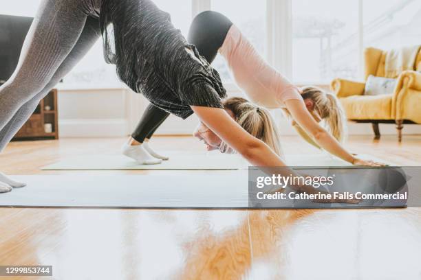 two woman perform yoga in a home environment - downward facing dog position stock pictures, royalty-free photos & images