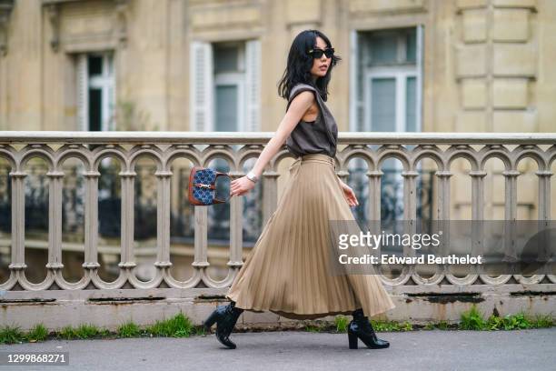 Fashion blogger Xiayan wears sunglasses from Bottega Veneta, a gray tank top from Copenhagen Muse, a beige pleated long skirt from Copenhagen Muse, a...