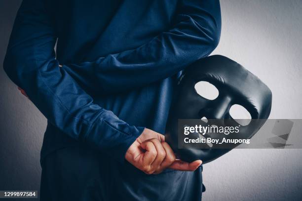 mystery man holding and hide the hacker mask behind his back. - anonymous mask photos et images de collection
