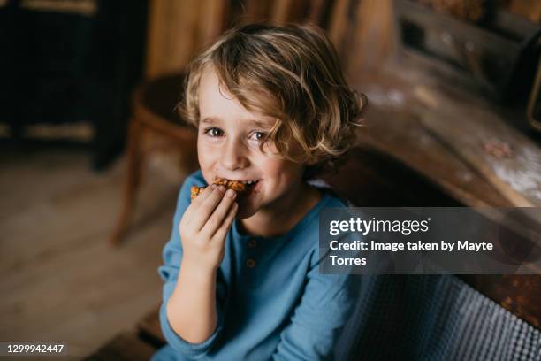 boy eating cookies and looking at camera sitting on a table in a cabin kitchen - kekse stock-fotos und bilder