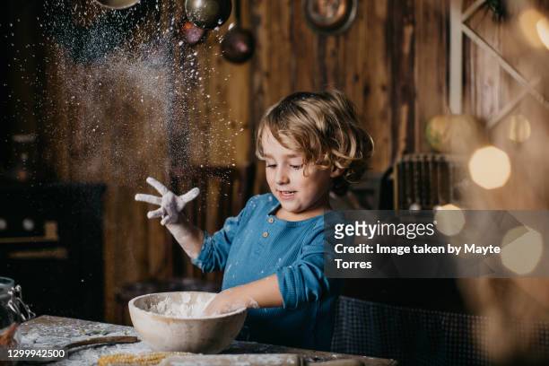 boy in a cabin kitchen playing and throwing flour to the air - kids baking stock-fotos und bilder
