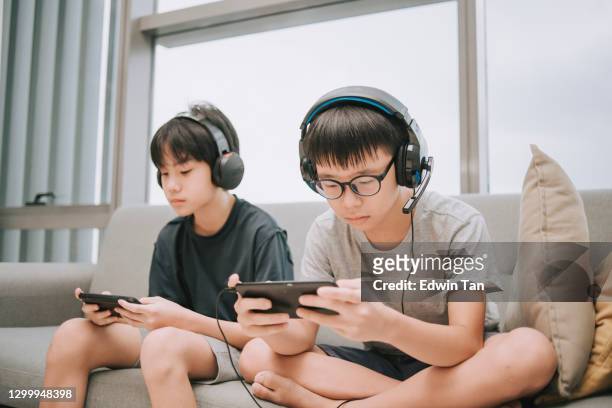 スマートフォン接続を使用してリビングルームでヘッドセットでマルチプレイヤーオンラインゲームをプレイアジアの中国の兄弟 - マッチ ストックフォトと画像