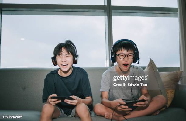 2 asian chinese sibling brother sitting on sofa playing online video games with headset in living room during weekend - boy playing stock pictures, royalty-free photos & images